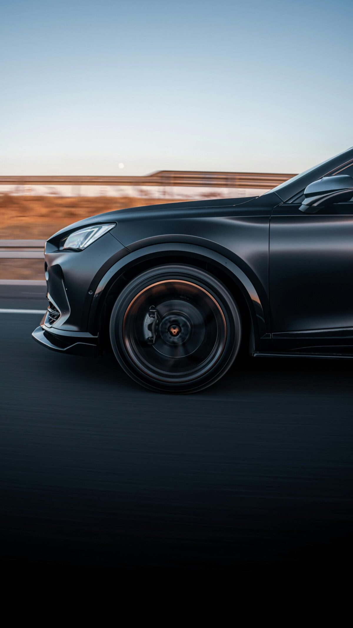A side profile of a black sports sedan with black wheels driving on a highway with a desert landscape in the background after an engine warning light repair.